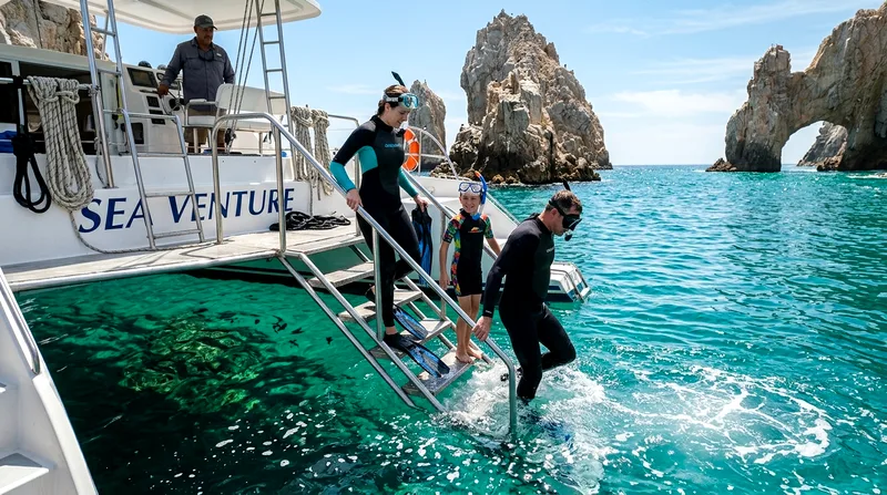 Snorkelers entering water from catamaran platform near Pelican Rock with El Arco in distance.