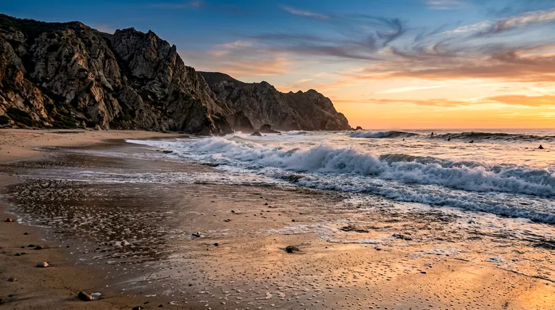 Todos Santos beach with Pacific surf and rocky cliffs at sunset.